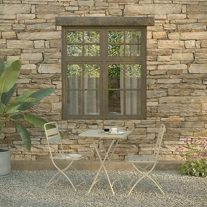 Feros Balkonmöbel-Set Breeze - 3 -tlg., Metall, Beige - Ein heller Gartentisch mit zwei passenden Stühlen vor einer Steinwand, einladend für eine entspannte Pause im Freien.
