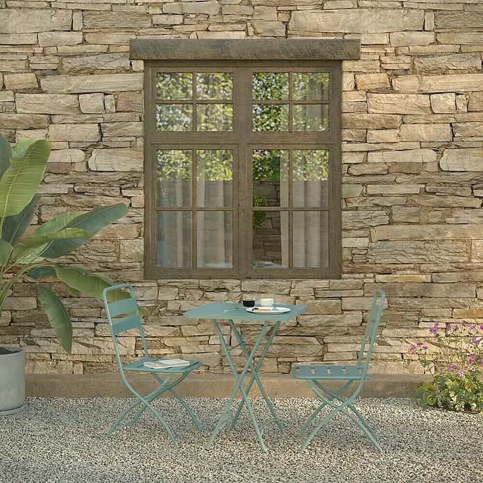 Feros Balkonmöbel-Set Breeze - 3 -tlg., Metall, Blau - Draußen sitzen: Ein türkisfarbener Gartentisch und Stühle vor einer Steinmauer und einem Fenster laden zum Verweilen ein.