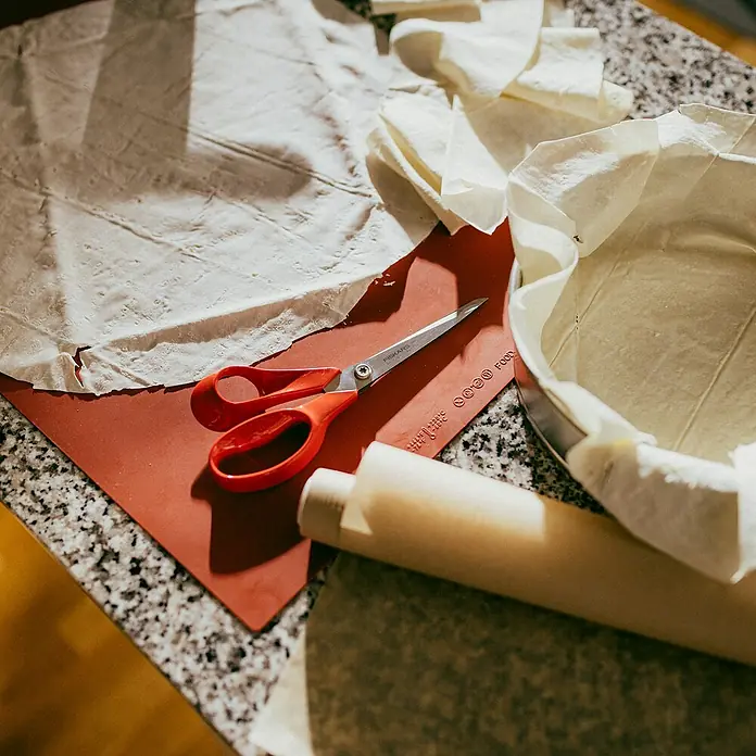 Fiskars Universalschere Classic - Länge: 21 cm, Rot - Nahaufnahme von Backutensilien wie Teig, Schere, Nudelholz und Kuchenform auf einer Küchentheke.