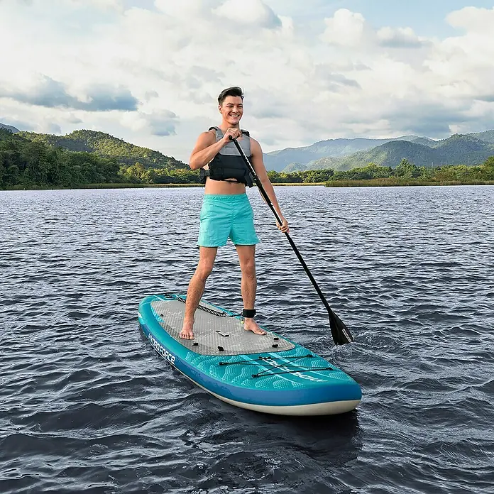 Bestway Hydro Force SUP-Board-Set Aqua Drifter™ mit Sitz - L x B x H: 335 x 91,5 x 15 cm, Nutzlast: 150 kg, Aufblasbar, Grün - Ein Mann paddelt auf einem Hydroforce-Stand-Up-Paddleboard auf einem ruhigen See mit Bergen im Hintergrund.