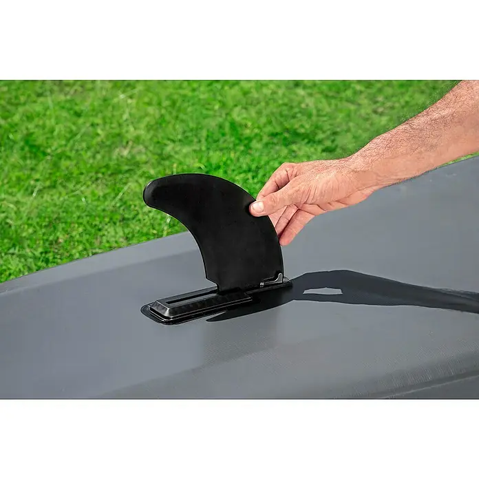 Bestway Hydro Force Kajak Ventura Elite™ X2 - L x B: 330 x 86 cm, Nutzlast: 200 kg, Geeignet für: 2 Personen - Eine schwarze Surfbrettfinne wird in eine Halterung auf einem Surfbrett eingesetzt, der grüne Rasen im Hintergrund sorgt für Kontrast.