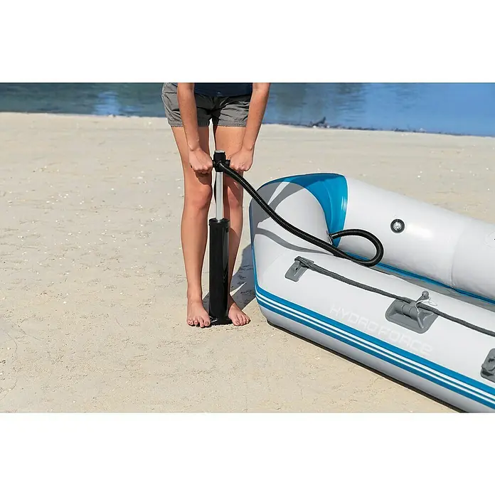 Bestway Hydro Force Schlauchboot Caspian - L x B x H: 230 x 130 x 33 cm, Geeignet für: 2 Personen, Nutzlast: 258 kg - Eine Person pumpt ein Hydro Force Schlauchboot am Strand mit einer Luftpumpe auf. Das Boot ist weiß mit blauen Akzenten.