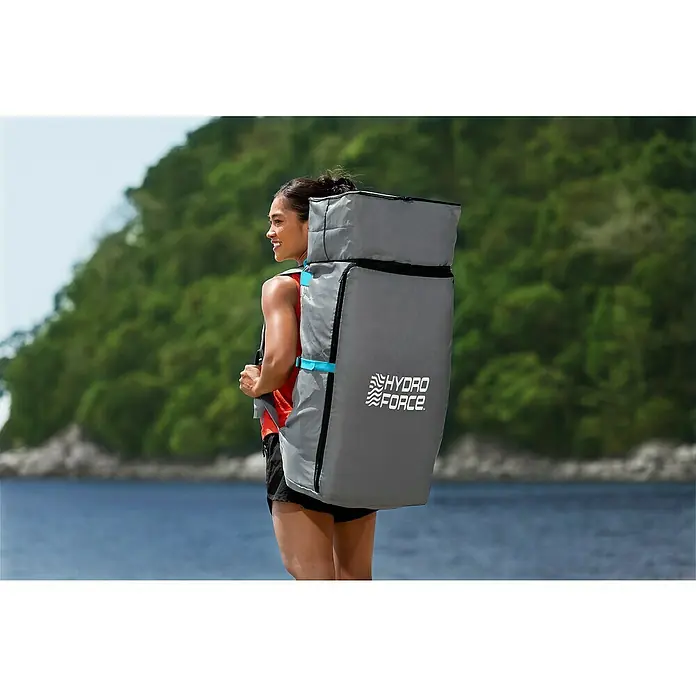 Bestway Hydro Force SUP-Board Aqua Glider™ - L x B x H: 320 x 79 x 12 cm, Nutzlast: 110 kg, Aufblasbar - Frau trägt einen grauen Hydro Force Rucksack vor einem Gewässer, ideal für Wassersportausrüstung, praktisch und stilvoll designt für Outdoor-Abenteuer.