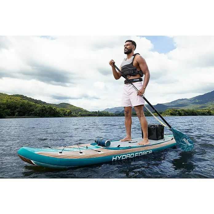 Bestway Hydro Force SUP-Board-Set Freesoul Elite™ mit Sitz - L x B x H: 335 x 84 x 15 cm, Nutzlast: 150 kg, Aufblasbar, Blau/Braun - Ein Mann paddelt auf einem Hydro-Force SUP-Board auf einem See. Das Board ist blaugrün mit einem Holzmuster.
