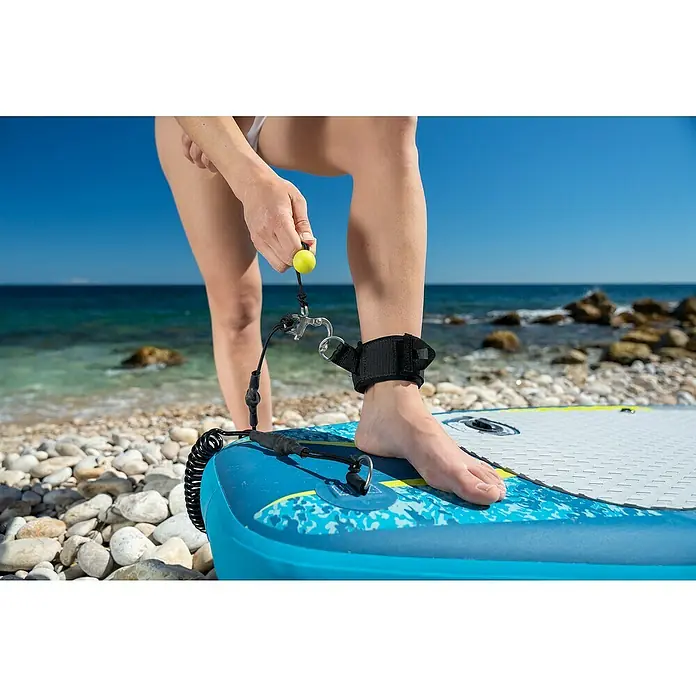 Bestway Hydro Force SUP-Board-Set Aqua Drifter™ View - L x B x H: 335 x 91,5 x 15 cm, Nutzlast: 140 kg, Aufblasbar, Grau/Blau - Nahaufnahme einer Person, die an einem sonnigen Strand eine Paddelbrett-Leine an ihrem Knöchel befestigt.