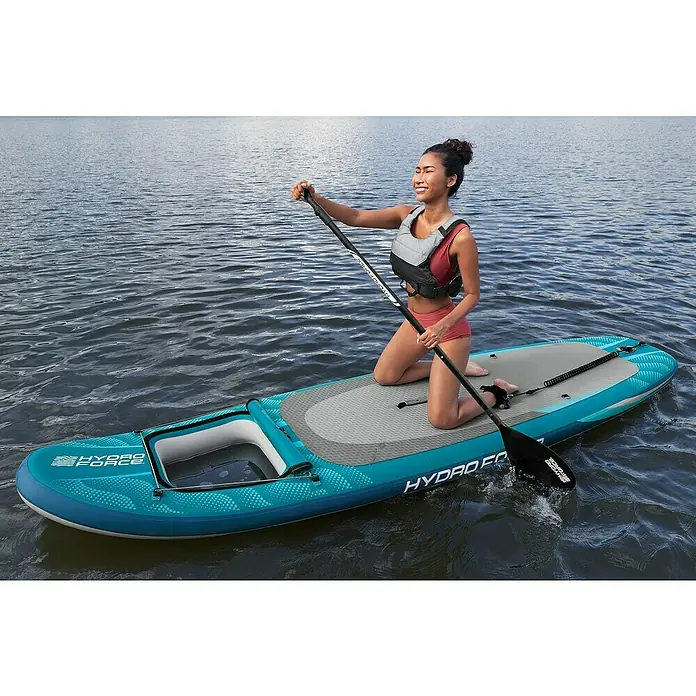 Bestway Hydro Force SUP-Board-Set Aqua Drifter™ View - L x B x H: 335 x 91,5 x 15 cm, Nutzlast: 140 kg, Aufblasbar, Grau/Blau - Frau auf einem Hydro-Force SUP-Board auf dem Wasser. Das Board ist blaugrün mit grauen Details und hat einen Sitzbereich.