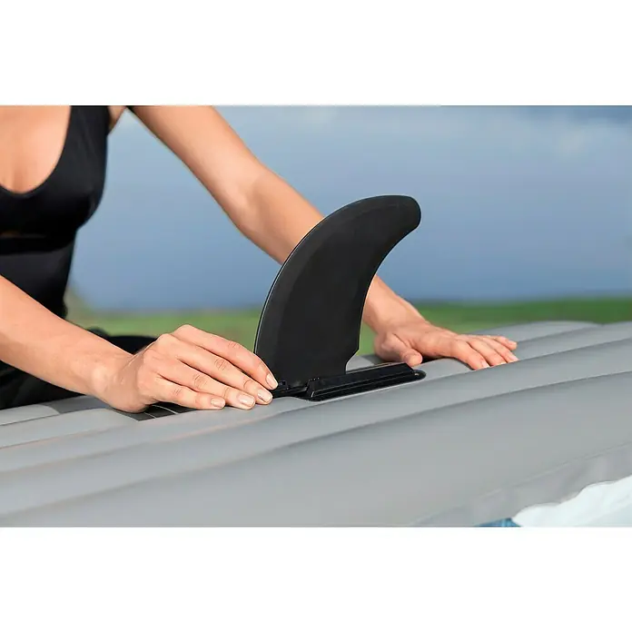 Bestway Hydro Force Kajak Rapid X1 - L x B: 290 x 91 cm, Nutzlast: 120 kg, Geeignet für: 1 Person - Nahaufnahme einer Person, die eine schwarze Finne an einem grauen Stand-Up-Paddleboard befestigt. Fokus auf die Befestigung der Finne.