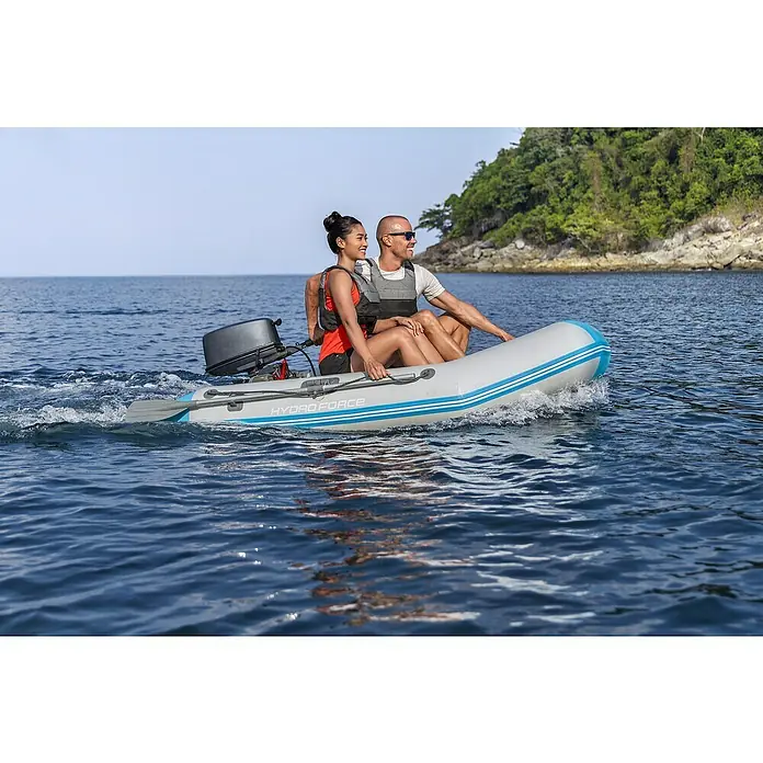Bestway Hydro Force Schlauchboot-Set Corinth Elite™ - L x B x H: 230 x 130 x 33 cm, Geeignet für: 2 Personen, Nutzlast: 280 kg - Ein graues Hydro-Force-Schlauchboot mit blauem Akzent fährt mit zwei Personen auf dem Wasser, angetrieben von einem Motor.
