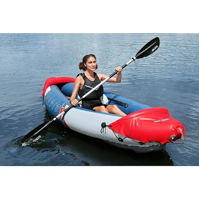 Bestway Hydro Force Kajak Rapid X1 - L x B: 290 x 91 cm, Nutzlast: 120 kg, Geeignet für: 1 Person - Eine Frau paddelt mit einem Hydro-Force Kajak auf dem Wasser. Das Kajak ist rot, blau und grau und hat eine Paddel.
