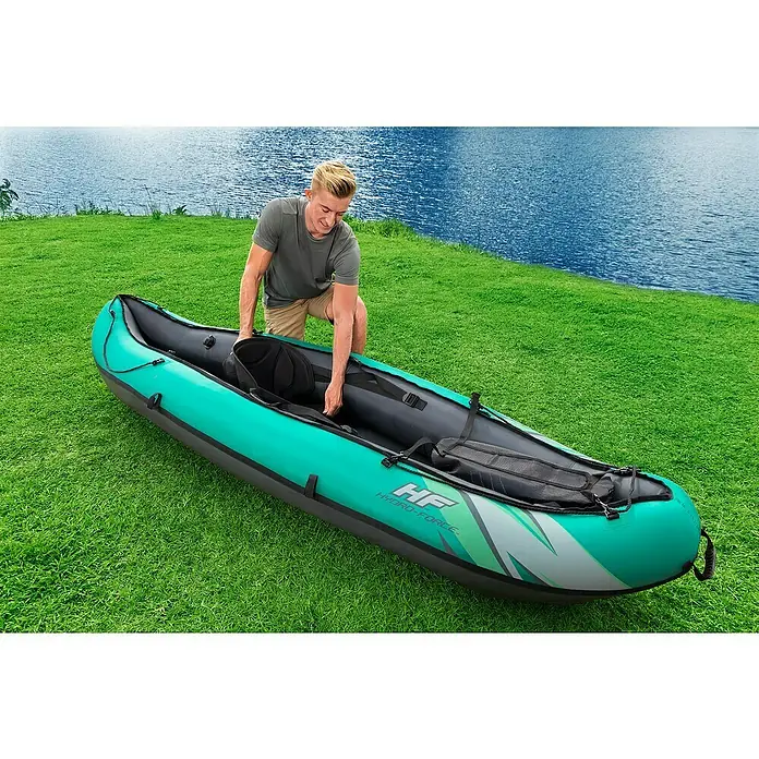 Bestway Hydro Force Kajak Ventura Elite™ X1 - L x B: 280 x 86 cm, Nutzlast: 130 kg, Geeignet für: 1 Person - Ein Mann bereitet ein aufblasbares Hydro-Force Kajak am Ufer eines Sees vor. Das Kajak ist grün und grau mit dem Logo gut sichtbar.