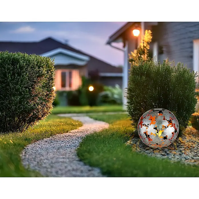 Globo Solar-Dekoleuchte Ahornblätter - Lichtfarbe: Warmweiß, LED, Höhe: 370 mm - Außenaufnahme einer solarbetriebenen Gartenkugel-Leuchte mit filigranen Ausschnitten, die warmes Licht in einem gepflegten Garten verbreitet.