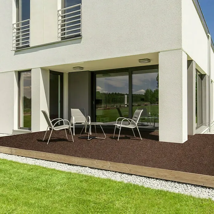 Rasenteppich Farbwunder - 1.800 x 200 cm, Braun, Mit Drainagenoppen - Terrasse mit braunem Belag vor einem modernen Haus mit Garten, ausgestattet mit eleganten Gartenmöbeln für entspannte Stunden im Freien.