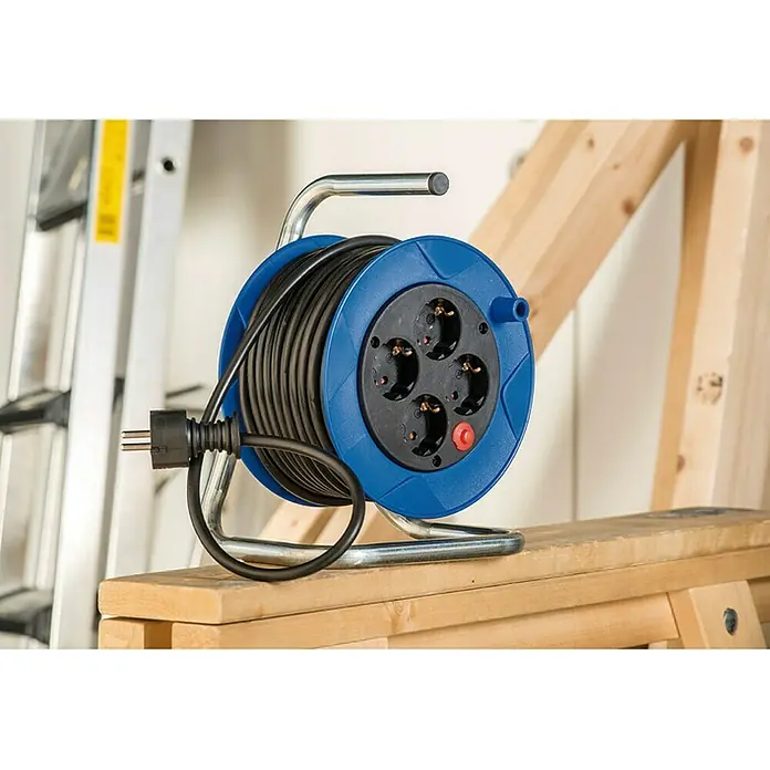 Brennenstuhl Kabeltrommel - Spezialkunststoff, 15 m, H05VV-F, IP20 - Blaue Kabeltrommel mit schwarzem Kabel und vier Steckdosen auf einem Holzbock, mit Leiter im Hintergrund für Heimwerker- und Bauprojekte.