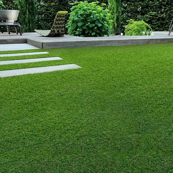 Kunstrasen Marbella - 2.000 x 100 cm, Grün - Bild einer grünen Rasenfläche im Garten mit Steinplatten und einer Terrasse mit Gartenmöbeln im Hintergrund.