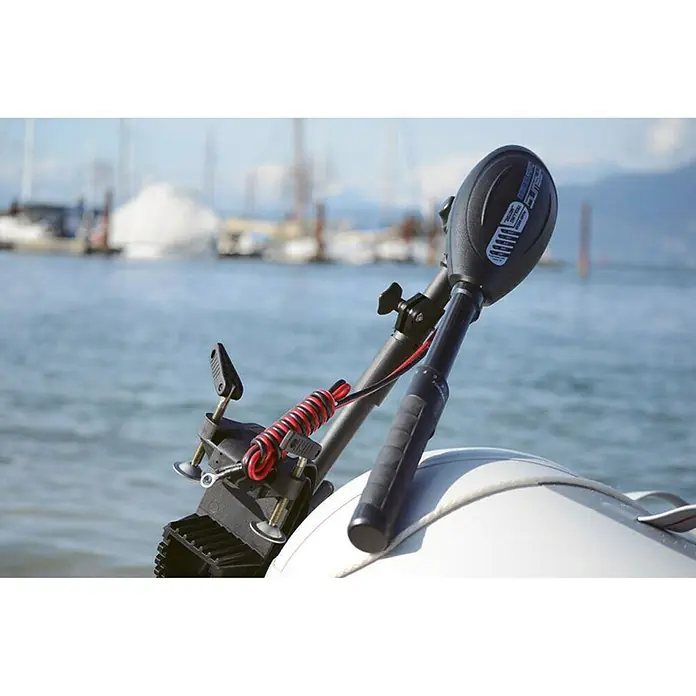 Hidea Motor fueraborda 2,5 HP - 1,8 kW, Control de timón, Eje corto - La imagen muestra un motor de barco eléctrico montado en la parte trasera de una pequeña lancha inflable, con un mar y montañas al fondo.