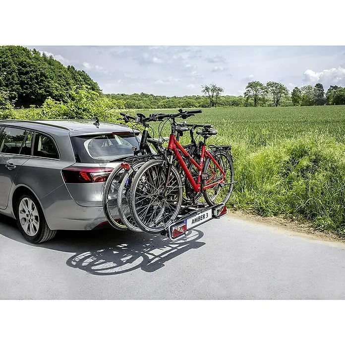 Eufab Fahrradträger Amber III - Geeignet für: 3 Fahrräder, Passend für: Fahrzeuge mit Anhängerkupplung - Heckansicht eines grauen Autos mit einem AMBER 3 Fahrradträger, auf dem zwei Fahrräder befestigt sind, vor einer grünen Landschaft.