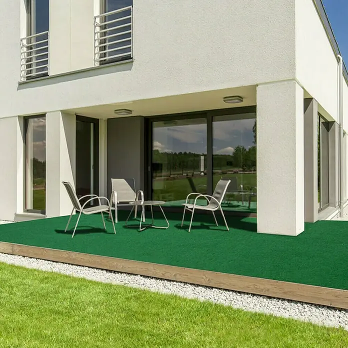 Rasenteppich Farbwunder - 300 x 200 cm, Grün, Mit Drainagenoppen - Einladende Terrasse mit Kunstrasen, umgeben von einem modernen Haus. Perfekt für entspannte Stunden im Freien.