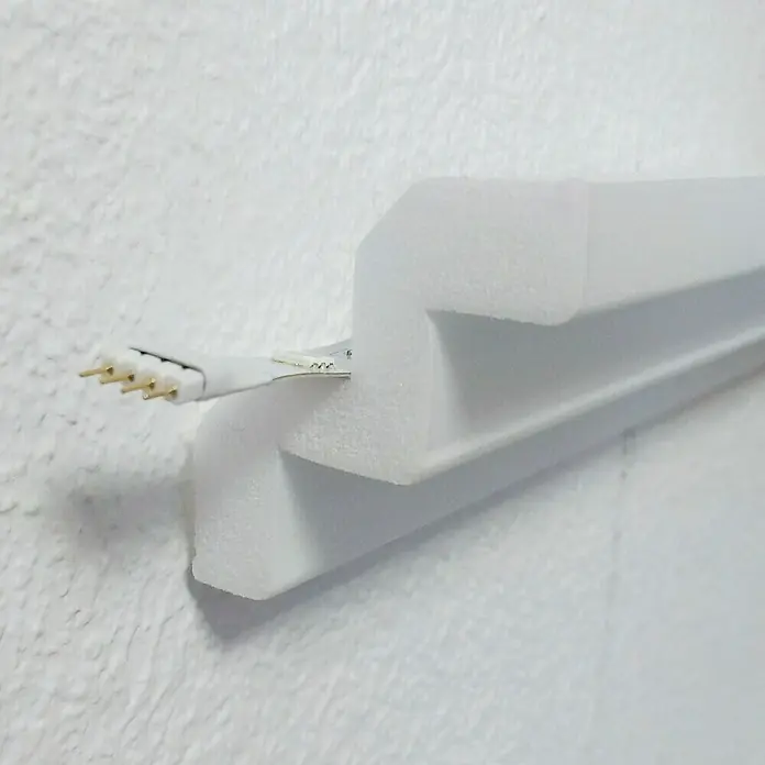 Zierprofil Modern T 70 - 200 x 5 x 5 cm, XPS-Hartschaumplatten - Nahaufnahme einer weißen LED-Leuchte mit Stiftleiste, die an einer weißen Wand befestigt ist.