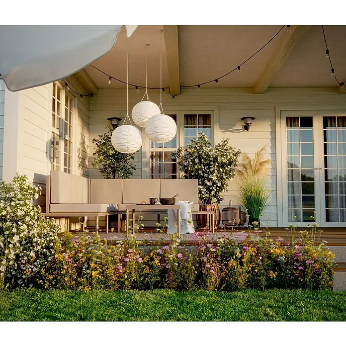 SENSUM Loungemöbel-Set Ankarsvik - 3 -tlg., Aluminium, Teak, Sandbraun - Außenaufnahme einer Terrasse mit grauer Eckcouch, drei Papierlaternen und Blumenbeeten, die eine gemütliche und einladende Atmosphäre schaffen.