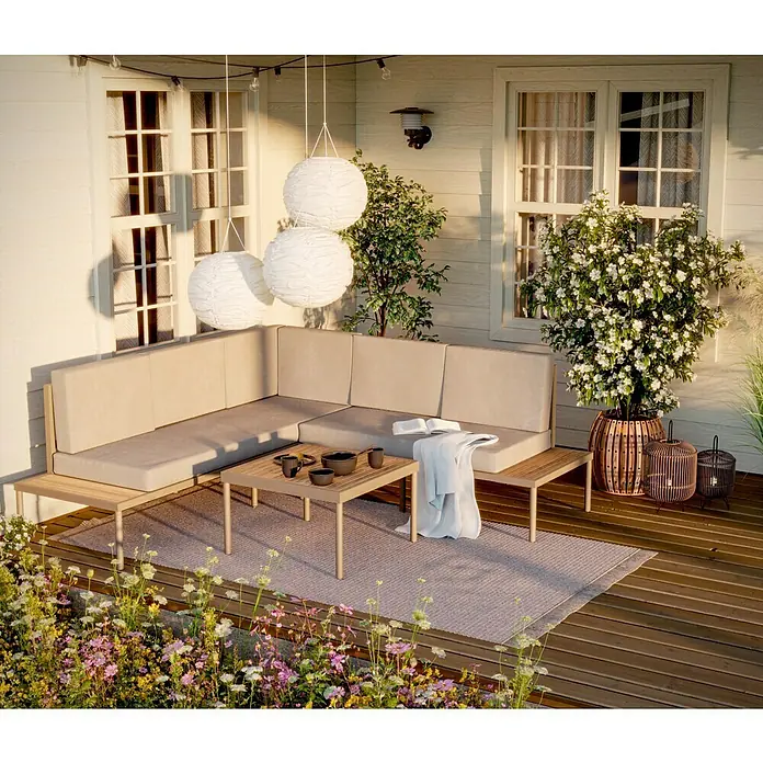 SENSUM Loungemöbel-Set Ankarsvik - 3 -tlg., Aluminium, Teak, Sandbraun - Gartenmöbel-Set mit Ecksofa, Tisch und Deko auf einer Holzterrasse mit Blumen im Vordergrund. Gemütliche Atmosphäre für den Außenbereich.