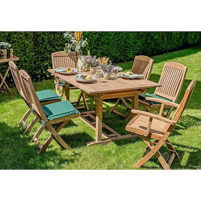 Kai Wiechmann Sitzauflage - Klappstuhl, L x B x H: 35 x 40 x 4 cm, Polyacryl, Dunkelgrün - Das Bild zeigt ein hölzernes Gartenset mit Tisch und Stühlen auf einem Rasen. Das Set ist mit Geschirr und Blumen dekoriert.