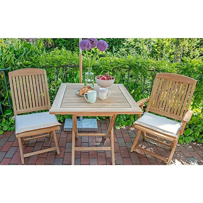 Kai Wiechmann Sitzauflage - Klappstuhl, L x B x H: 35 x 40 x 4 cm, Polyacryl, Naturweiß - Ein Gartentisch-Set mit zwei Stühlen auf einer Terrasse, dekoriert mit Blumen, Geschirr und Gebäck, umgeben von üppigem Grün.