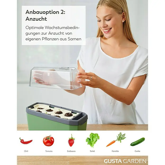 Gusta Garden Anzucht-Set Stadtkräutergarten Set - 6 -tlg., Dunkelgrau - Das Bild zeigt eine Frau, die einen Zimmergewächshaus-Aufsatz auf eine grüne Pflanzbox setzt, um optimale Anzuchtbedingungen zu schaffen.