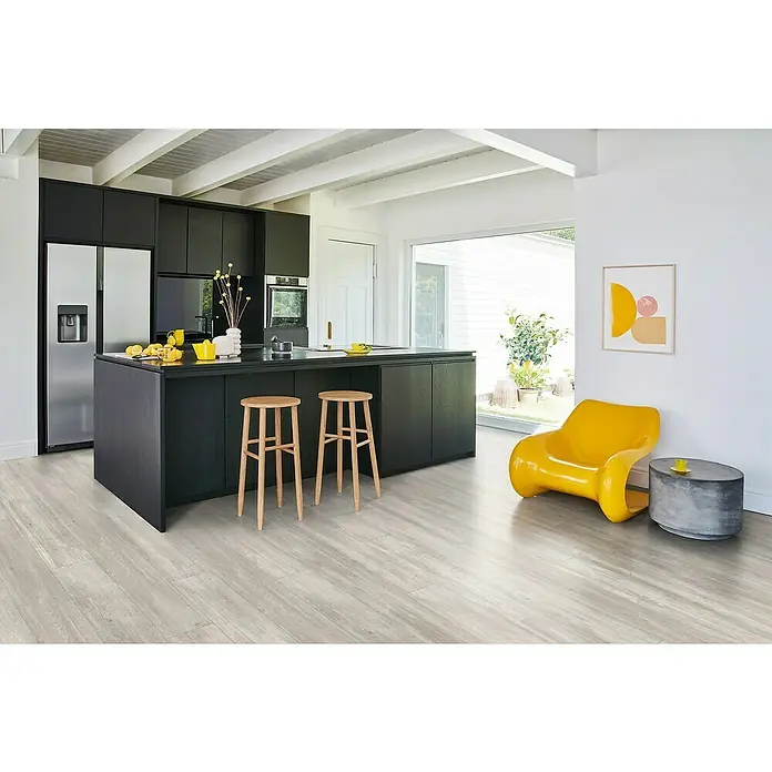 Parador Designbodenmuster Modular ONE Eiche - 200 x 194 x 8 mm, Landhausdiele, Eiche Nordic Grau - Helle Küche mit dunkler Kücheninsel, Holzhockern, gelbem Sessel und grauen Holzböden, die eine moderne und einladende Atmosphäre schaffen.
