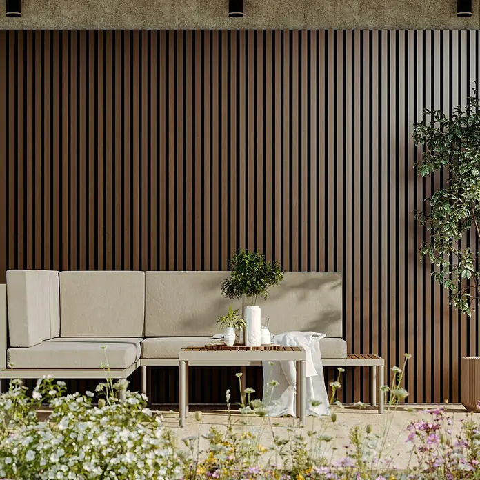 Wandpaneel Outdoor - Brown, WPC, 2.350 x 219 x 26 mm - Stilvolle Terrassengarnitur mit beigem Ecksofa und Holztisch vor einer modernen Holzpaneelwand. Pflanzen und Blumen im Vordergrund.