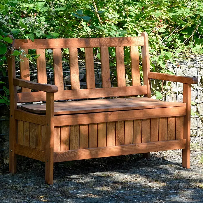 Dobar Gartenbank - B x T x H: 115 x 58 x 89 cm, Kiefer, Braun - Eine rustikale Gartenbank aus Holz mit Stauraum unter der Sitzfläche, umgeben von Grün.