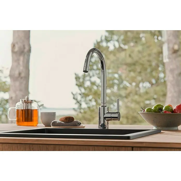 Hansa Vantis Spültischarmatur - Chrom, Glänzend - Nahaufnahme eines glänzenden Wasserhahns an einer Spüle, umgeben von Teekanne, Tasse, Schwamm und frischen Tomaten auf einer Holzoberfläche.