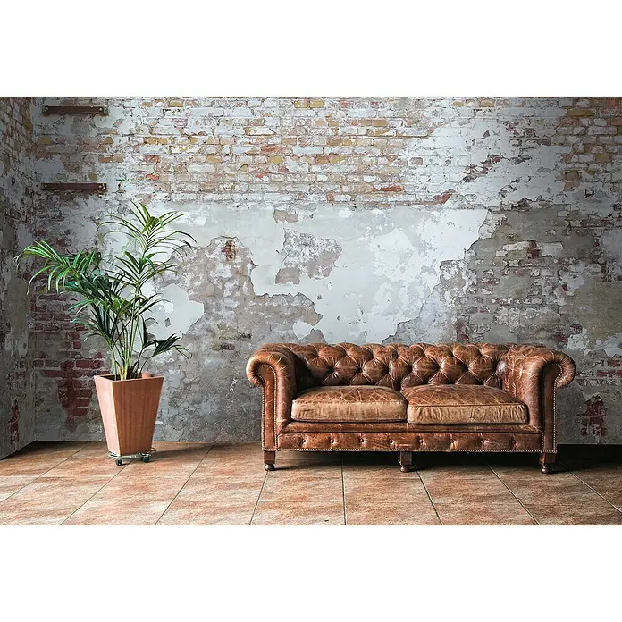 A.S. Création The Wall 2 Fototapete Ziegelsteinwand - B x H: 371 x 280 cm, Vlies - Elegante braune Chesterfield-Couch vor einer rustikalen Backsteinwand mit Topfpflanze. Die Couch lädt zum Entspannen ein.