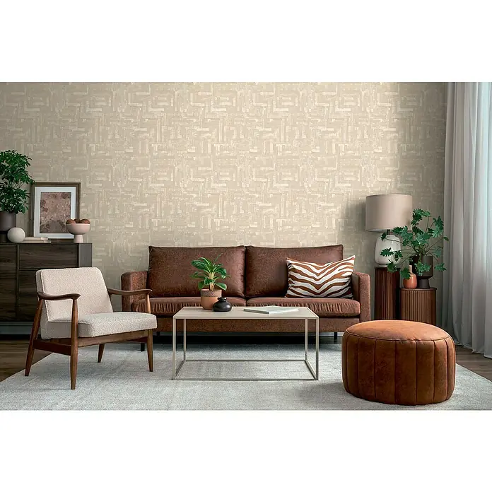 A.S. Création Metropolitan Stories Hot Spots Vliestapete Ethno - Beige-Creme-Grau, Grafisch, 10,05 x 0,53 m - Wohnzimmer mit braunem Sofa, Sessel und Pouf auf einem hellen Teppich vor einer beigen, gemusterten Wand.