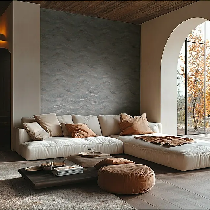 A.S. Création Metropolitan Stories Hot Spots Vliestapete Wellengrafik - Grau-Braun-Metallic, Wellen, 10,05 x 0,53 m - Ein stilvolles Wohnzimmer mit einem cremefarbenen Ecksofa, einem dunklen Couchtisch und einem braunen Pouf auf einem Teppich.