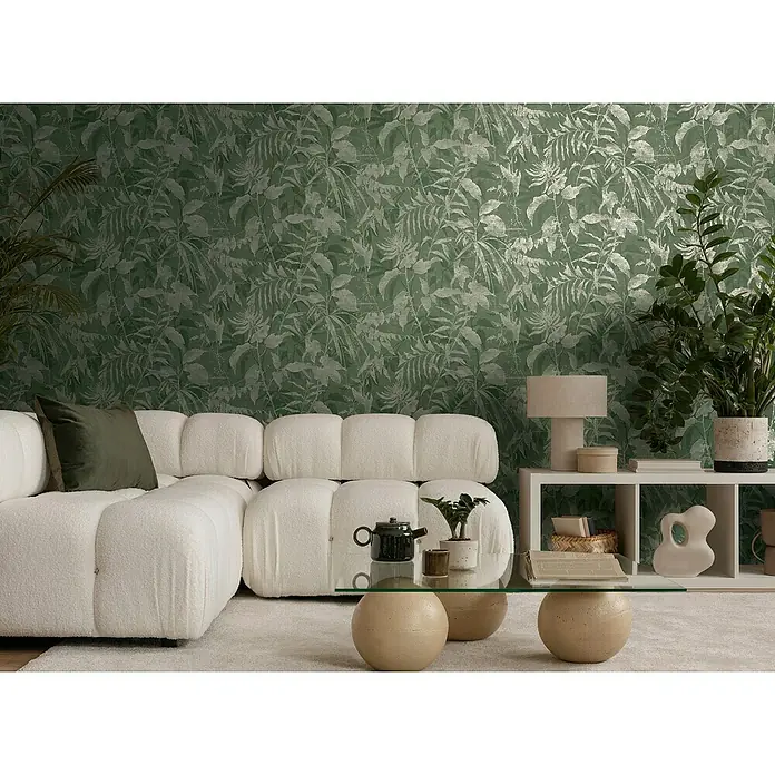 A.S. Création Metropolitan Stories Hot Spots Vliestapete Dschungel - Grün-Gold-Metallic, Floral, 10,05 x 0,53 m - Wohnzimmer mit modularem Bouclé-Sofa und Couchtisch mit kugelförmigem Sockel vor einer botanischen Tapete.