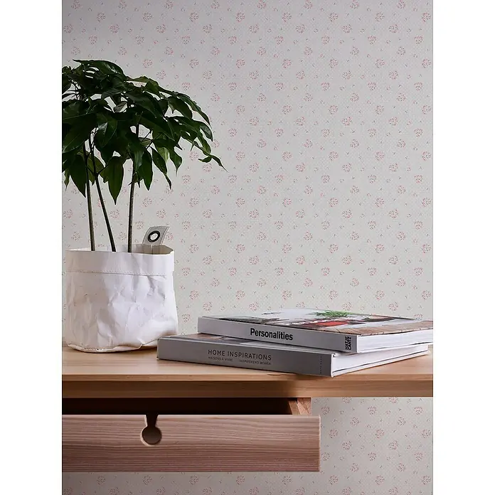 A.S. Création Maison Charme Vliestapete Blümchen - Hellgrau-Rot-Weiß, Floral, 10,05 x 0,53 m - Nahaufnahme eines Tisches mit Zimmerpflanze, Büchern und einer Schublade vor einer gemusterten Tapete.