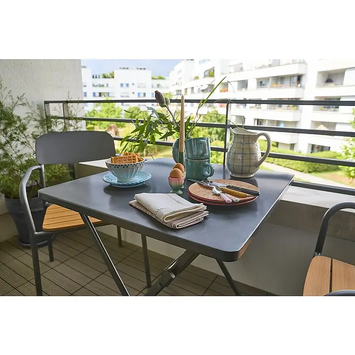 Sunfun Gastro Stapelstuhl - Stahl, Polywood, Stapelbar, Night-Grey, B x T x H: 57,5 x 53,5 x 83,5 cm - Esstisch auf einem Balkon mit Frühstück, inklusive Geschirr, Tassen, Eier und Waffeln, vor einem Hintergrund mit Wohngebäuden.