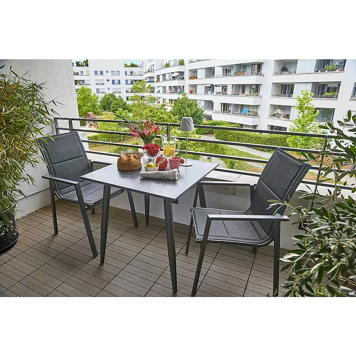 Sunfun Balkonmöbel-Set Solo/Maja II - 3 -tlg., Aluminium, Sintered Stone, Textilen, Night-Grey, Gartenstuhl stapelbar - Tischgruppe für den Balkon mit zwei grauen Stühlen und einem Tisch mit Dekorationen wie Blumen und Essen für ein entspanntes Frühstück im Freien.