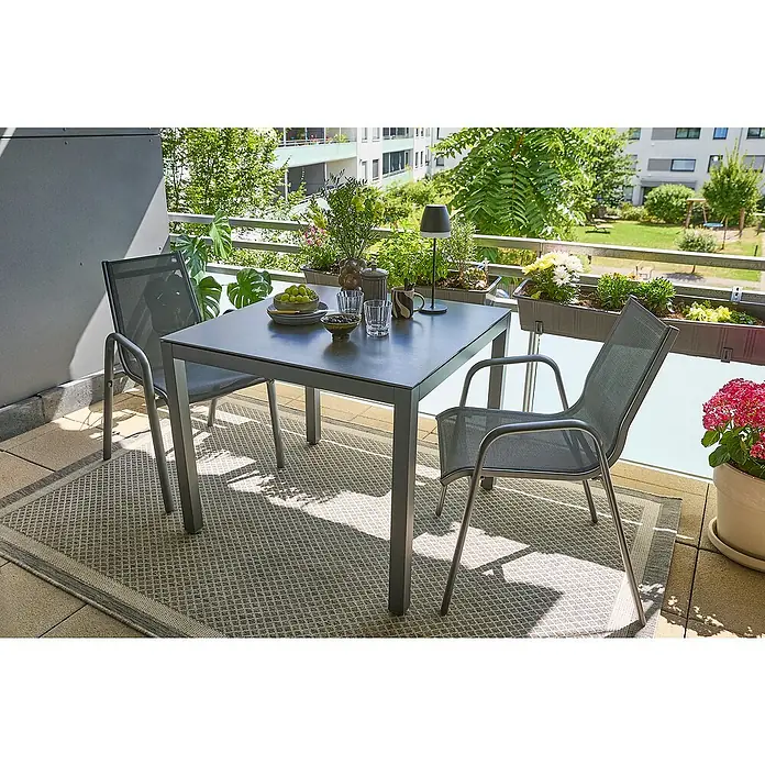 Sunfun Balkonmöbel-Set Maja/Gastro - 3 -tlg., Aluminium, Sintered Stone, Textilen, Grau, Gartenstuhl stapelbar - Ein grauer Gartentisch mit zwei Stühlen auf einem Balkon mit Pflanzen. Der Tisch bietet Platz für Speisen und Getränke im Freien.