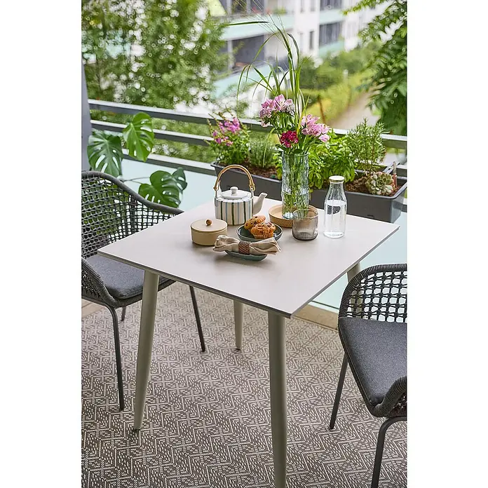 Sunfun Solo Balkontisch - L x B x H: 74 x 74 x 74 cm, Aluminium, Sintered Stone, Quadratisch, Light-Greige - Quadratischer Gartentisch mit grauem Musterteppich und Dekorationen wie Blumen und Geschirr für eine entspannte Atmosphäre im Freien.