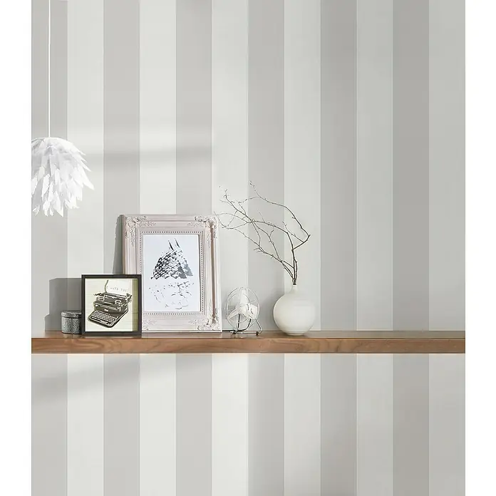 A.S. Création Maison Charme Vliestapete Blockstreifen - Grau-Creme-Weiß, Streifen, 10,05 x 0,53 m - Ein stilvolles Wandregal mit dekorativen Gegenständen wie Bilderrahmen, einer Vase und einem kleinen Ventilator vor einer gestreiften Tapete.