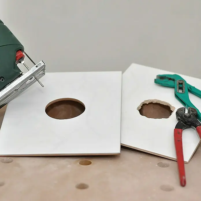Heka Fliesenfräser - Diamantbeschichtet - Zwei quadratische, weiße Holzplatten, eine mit sauberem Loch, die andere unsauber, umgeben von Werkzeug wie Stichsäge und Zangen.