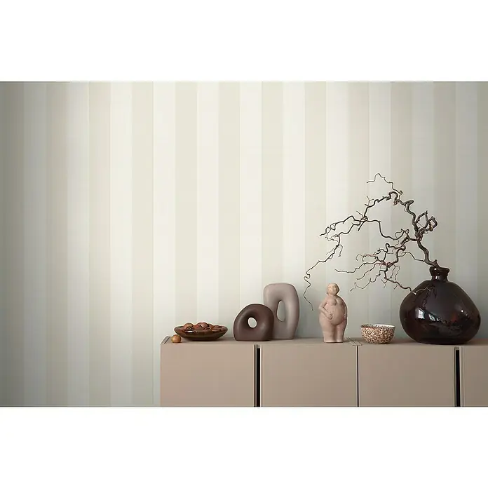 A.S. Création Maison Charme Vliestapete Blockstreifen - Beige-Weiß, Streifen, 10,05 x 0,53 m - Deko-Arrangement auf einem Sideboard vor gestreifter Tapete: Skulpturen, Schale mit Nüssen und eine Vase mit Zweigen für ein stilvolles Ambiente.