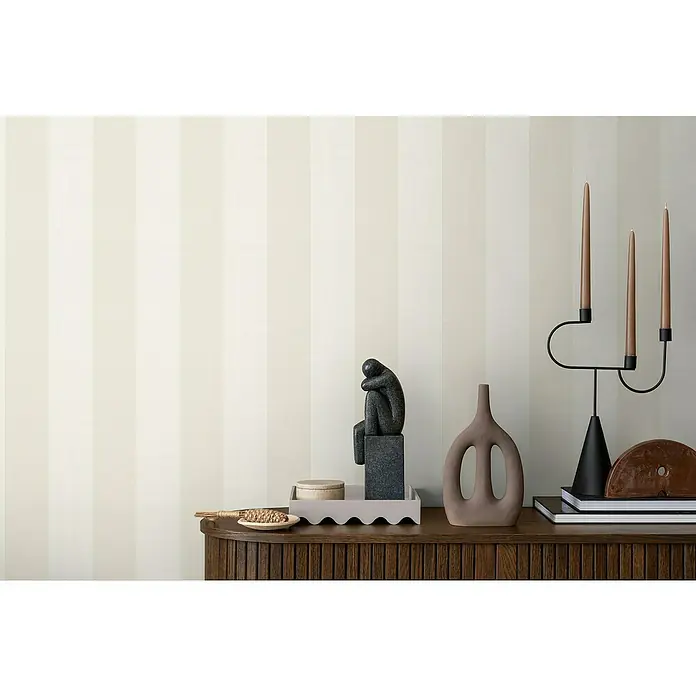 A.S. Création Maison Charme Vliestapete Blockstreifen - Beige-Weiß, Streifen, 10,05 x 0,53 m - Elegantes Interieur mit einem dunklen Holzschrank, darauf eine Skulptur, eine Vase und ein Kerzenständer mit schlanken, braunen Kerzen.