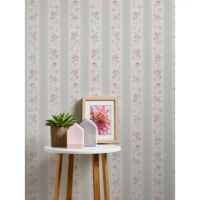 A.S. Création Maison Charme Vliestapete Vertikale Blümchen - Grau-Weiß-Violett, Floral, 10,05 x 0,53 m - Tisch mit Sukkulente, Deko-Häusern und gerahmtem Blumenbild vor einer Wand mit floralem Streifenmuster.