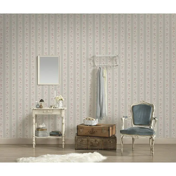 A.S. Création Maison Charme Vliestapete Vertikale Blümchen - Grau-Weiß-Violett, Floral, 10,05 x 0,53 m - Einrichtungsidee mit einem blauen Sessel, einem Tisch mit Spiegel und Gepäckstücken in einem Raum mit floral gemusterter Tapete.