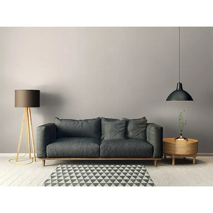 A.S. Création Maison Charme Vliestapete - Grau-Weiß, Streifen, 10,05 x 0,53 m - Geräumiges, dunkelgraues Sofa mit weichen Kissen, ergänzt durch einen eleganten Beistelltisch und eine stilvolle Stehlampe, ideal für modernes Wohnen.