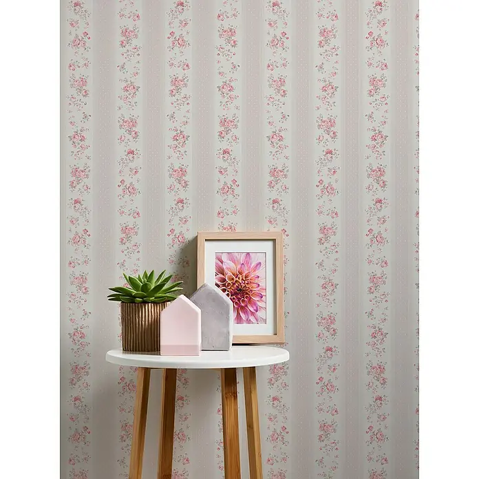 A.S. Création Maison Charme Vliestapete Vertikale Blümchen - Grau-Rot-Weiß, Floral, 10,05 x 0,53 m - Nahaufnahme von Blumen-Tapetenmustern, ein goldener Pflanztopf, eine rosa Hausdeko und gerahmtes Blumenbild auf einem kleinen, runden, weißen Tisch.