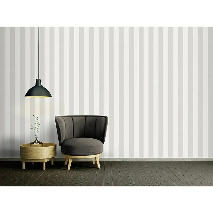 A.S. Création Maison Charme Vliestapete Blockstreifen - Grau-Creme-Weiß, Streifen, 10,05 x 0,53 m - Elegantes Interieur mit einem stilvollen grauen Sessel, einem Beistelltisch mit Dekoration und einer Hängelampe vor einer gestreiften Wand.