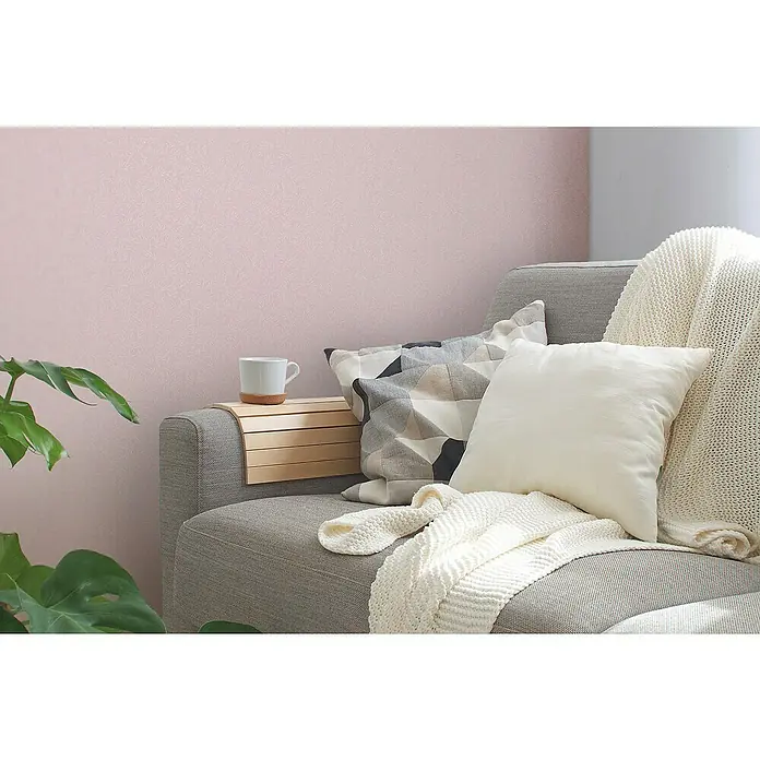 A.S. Création Maison Charme Vliestapete Ranke - Rosa-Weiß, Floral, 10,05 x 0,53 m - Nahaufnahme von einem grauen Sofa mit Kissen und einer Strickdecke, mit einer Ablage für eine Tasse.